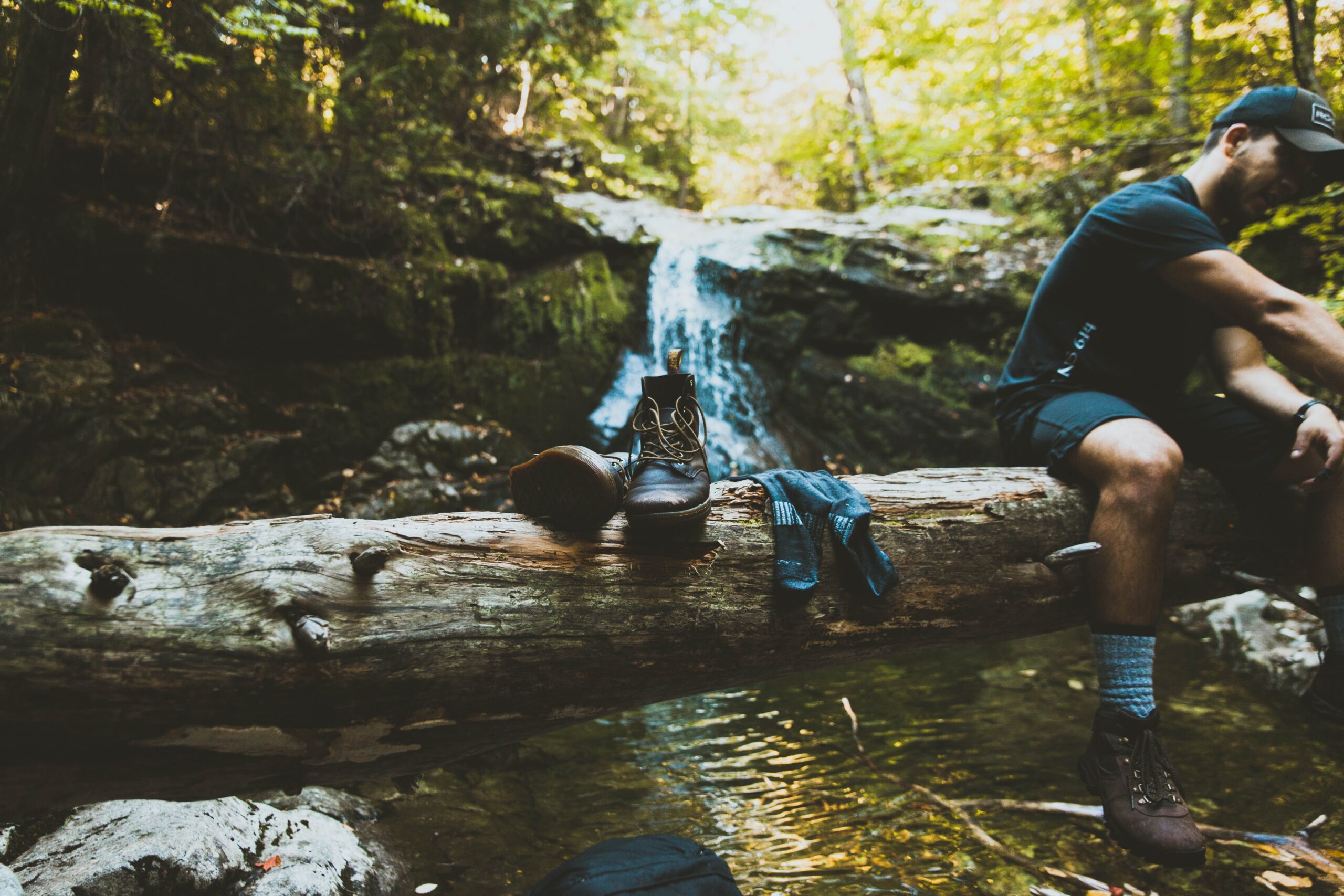 A man sitting on a tree log beside boots