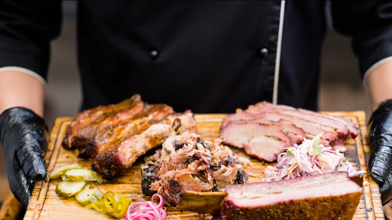 chef holding wooden board with smoked meat assortment, coleslaw salad, pickles