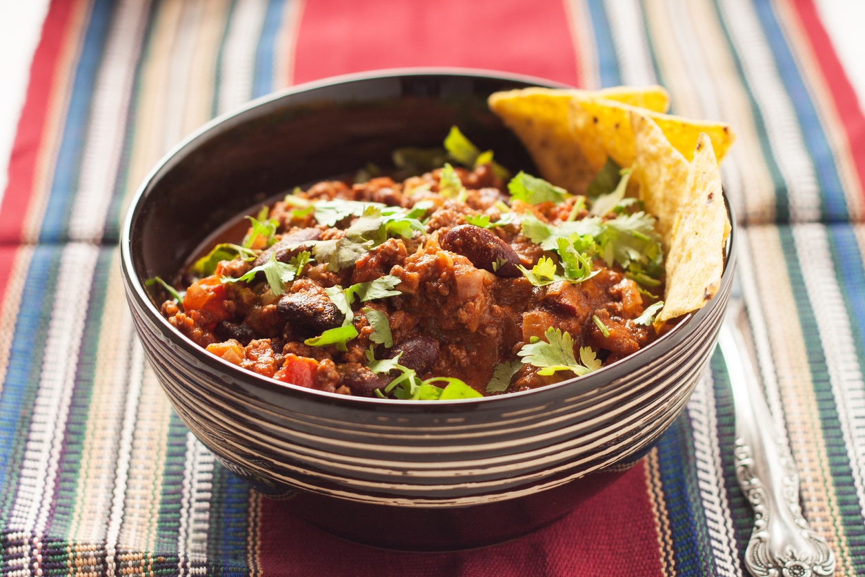 Chili con carne sprinkled with chopped cilantro served with tortilla chips in bowl