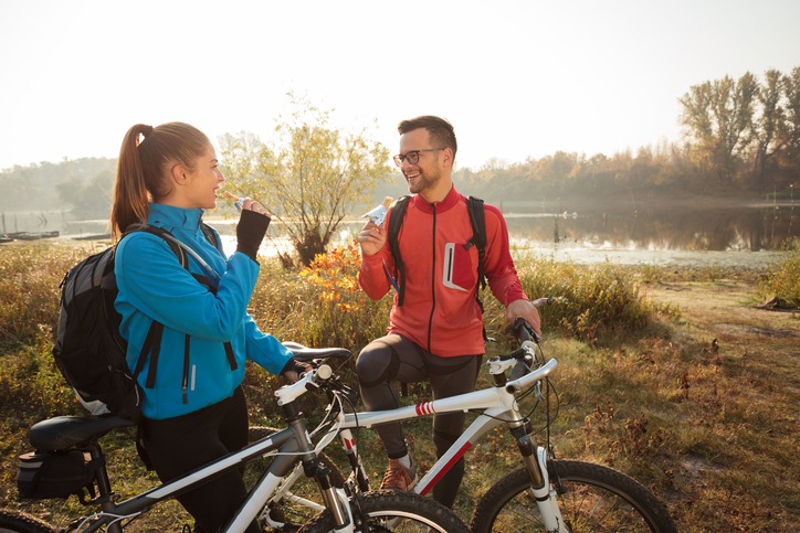 Young couple eating energy bars, resting beside their bikes during early morning mountain bike ride